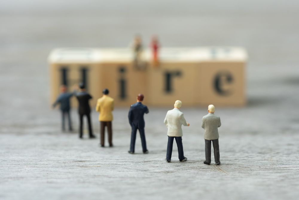 Miniature candidates lining up for wooden word block HIRE