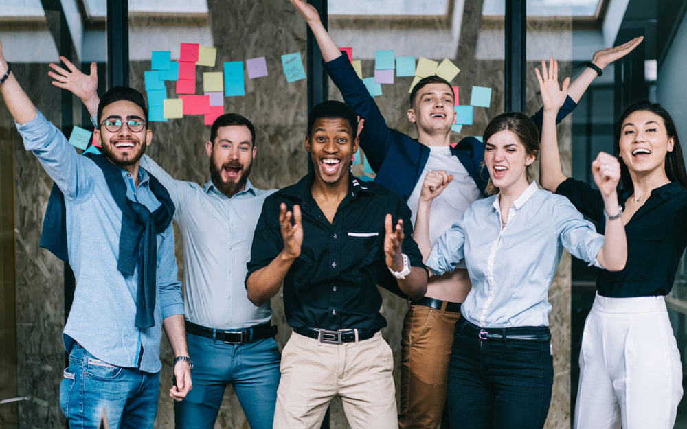 group of six young employees smiling and jumping in office 