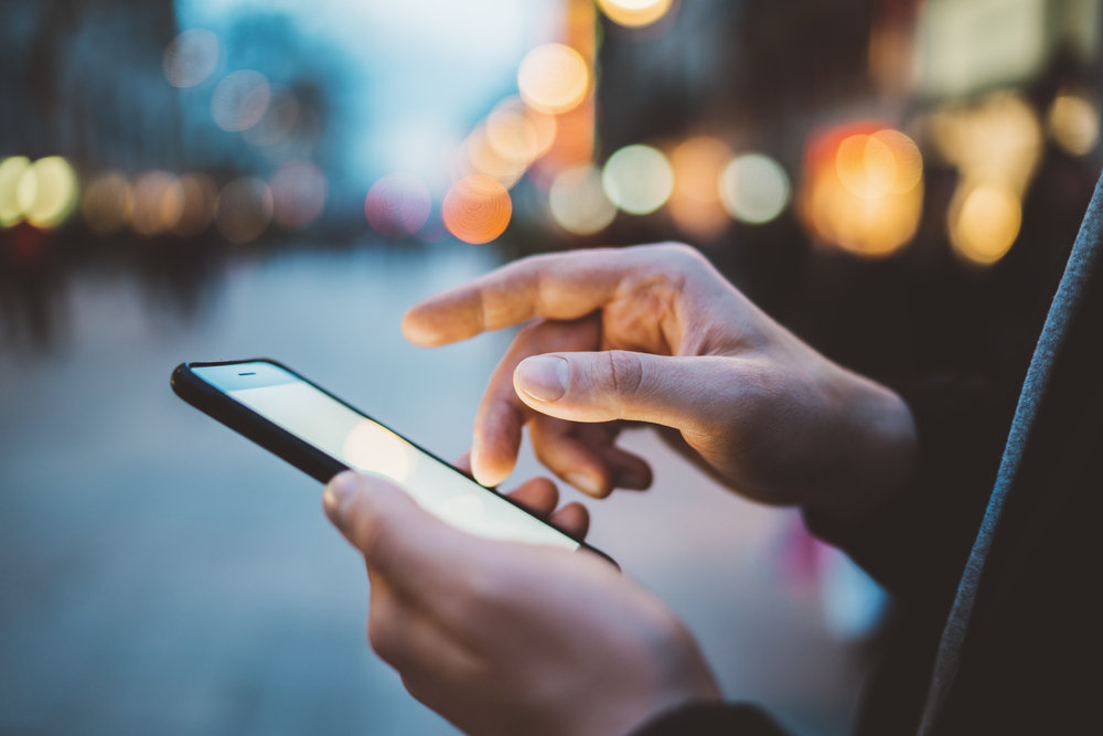 hand of male person holding a phone on street