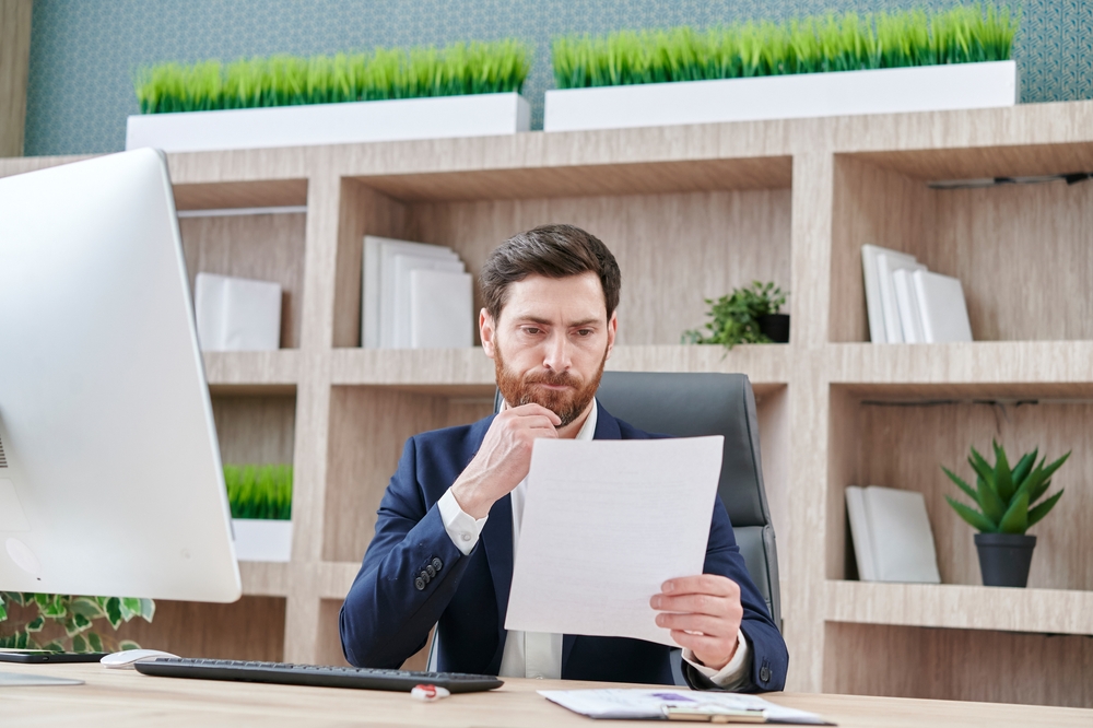 Male HR Recruiter thinking and looking at a resume while sitting in front of a desktop