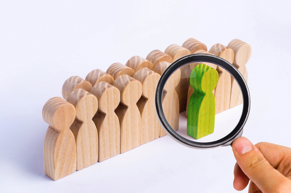 magnifying glass on wooden human figure of green color that stands out from the crowd