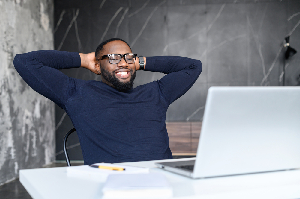 male hr recruiter sitting in front of laptop with his hands behind head