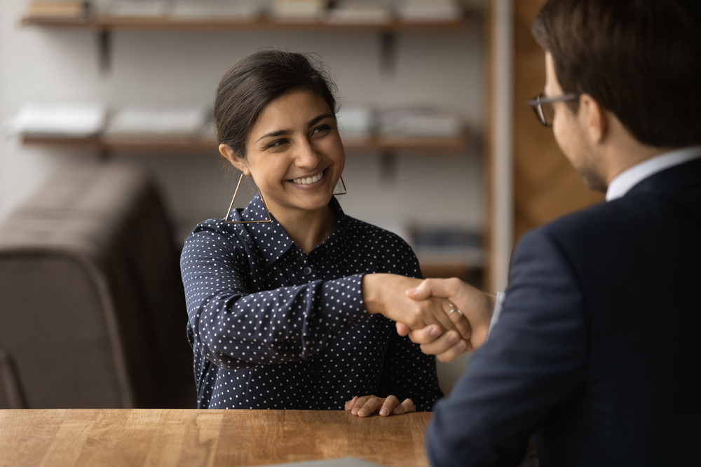 smiling young Indian female candidate while handshaking a male recruiter