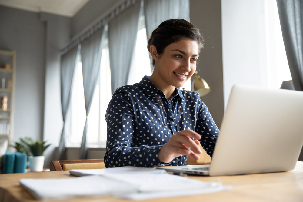 a smiling woman sitting and looking at laptop screen