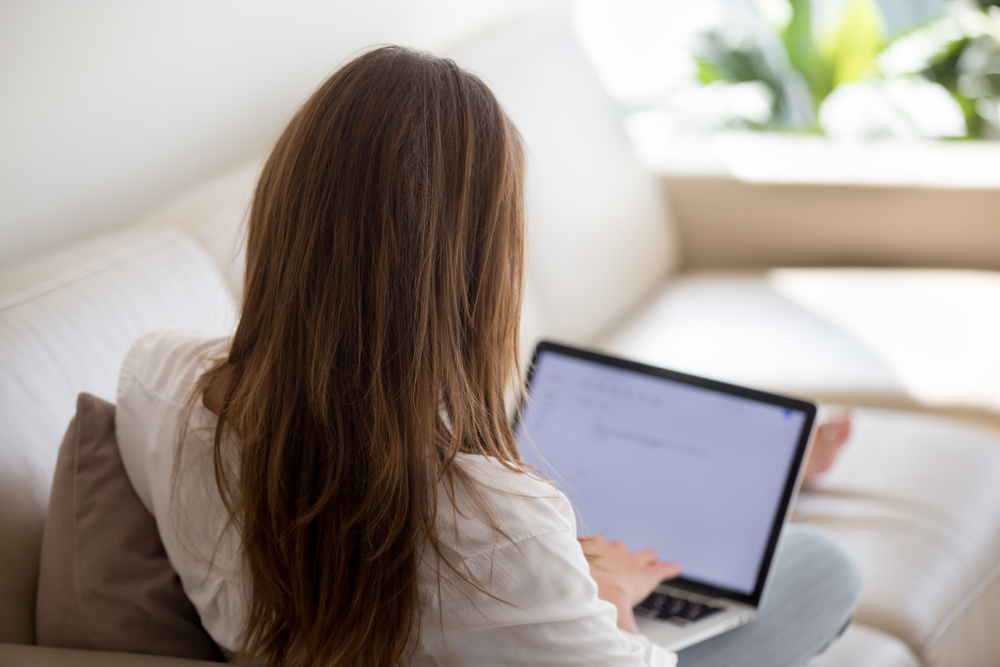 a woman sitting on couch while typing a letter on laptop