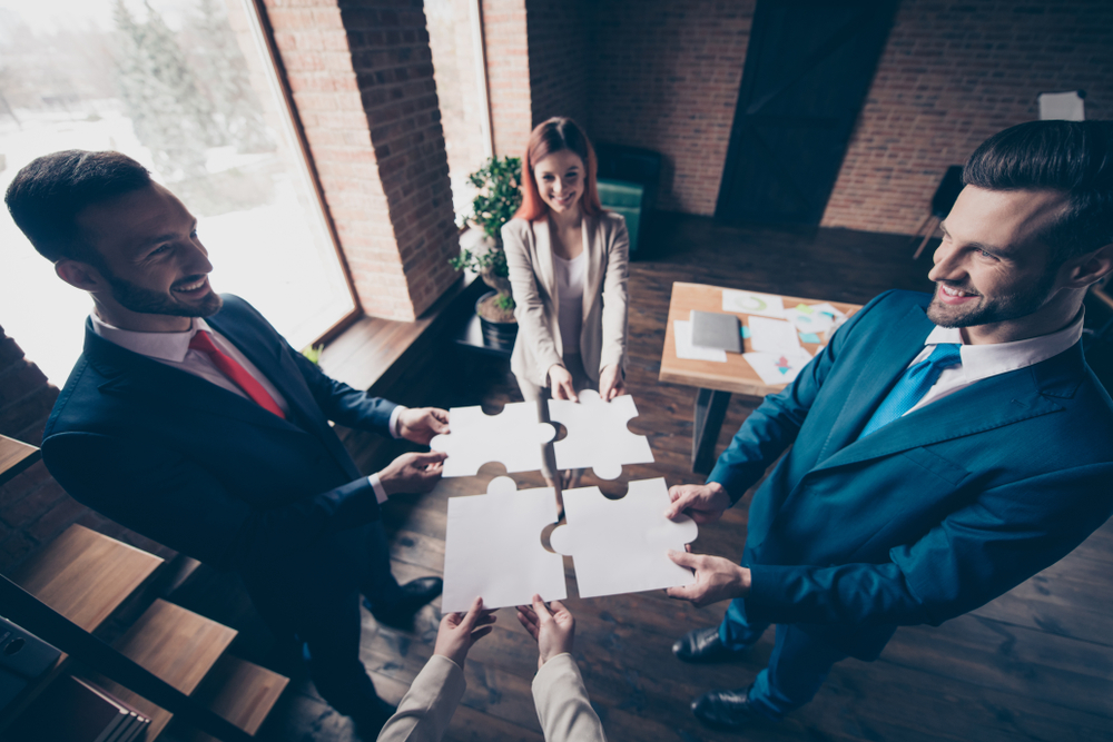 four smiling employees connecting big pieces of puzzle