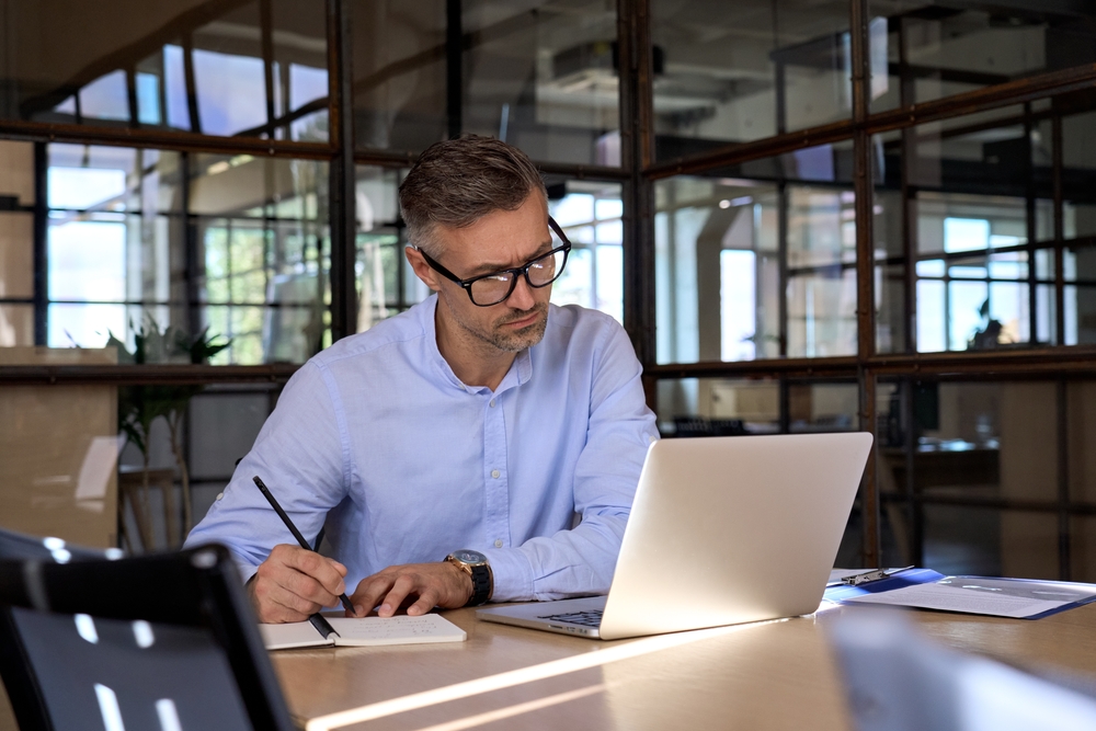 male recruiter writing on notepad while looking at laptop screen