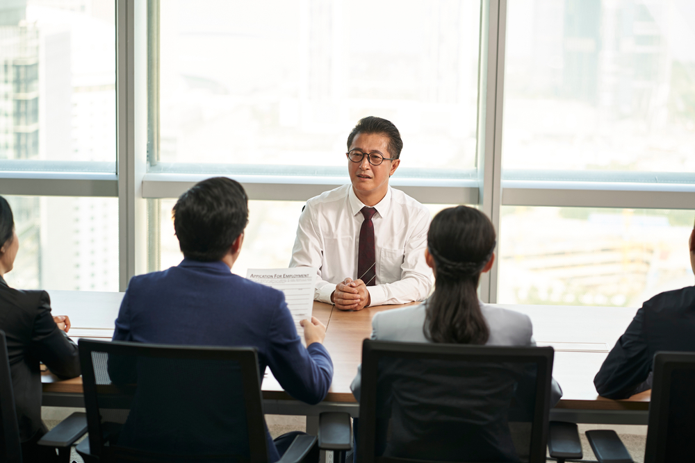 older asian man being interviewed by a group of young recruiters
